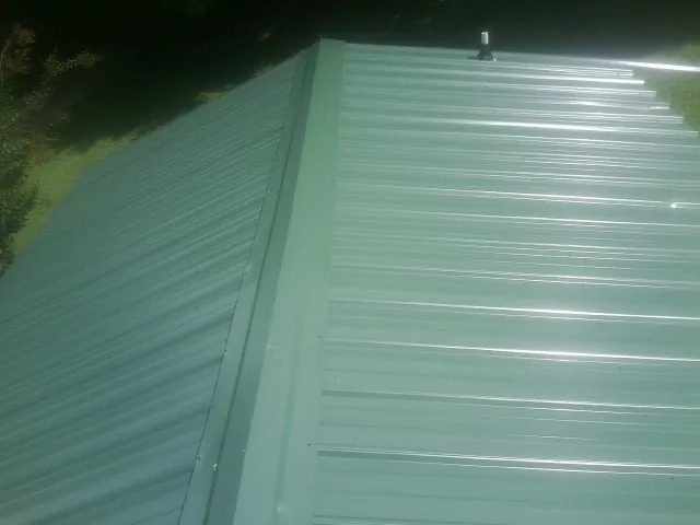 New green metal panels meeting at the ridge of a roof — Flat Roof Repair work by our crew in Loganville
