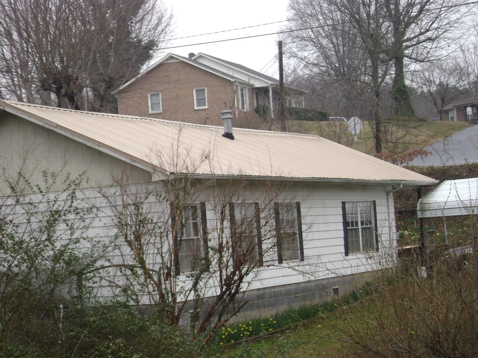 Tan metal roof on a white sided house set into a hillside — Commercial Roofing by Roofing Brothers in Loganville